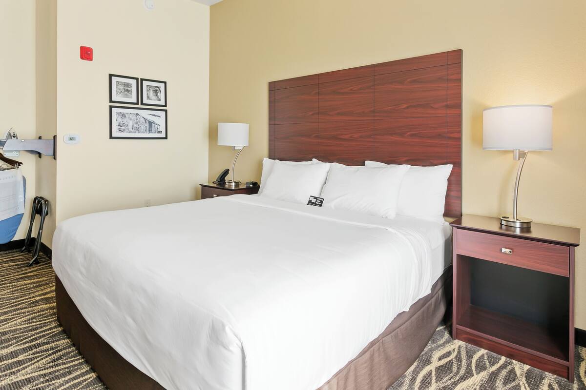 A hotel room with a large bed, a wooden headboard, a nightstand with a lamp, and a wall-mounted telephone.