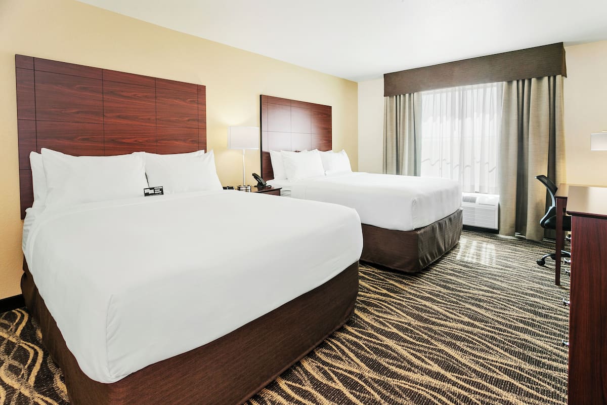 A hotel room with two beds, a desk, a chair, and a large window with curtains.