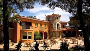 Un edificio de estilo mediterráneo con un patio, mesas al aire libre y una torre.
