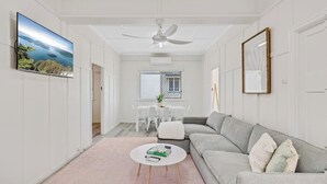 A modern living room with a grey sofa, a round coffee table, and a ceiling fan. There is a TV mounted on the wall and a framed picture above the sofa. - Sage Cottage! CBD Perfection! (East Toowoomba)