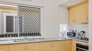 A kitchen with wooden cabinets, a double sink, a microwave, and an oven. - Sage Cottage! CBD Perfection! (East Toowoomba)