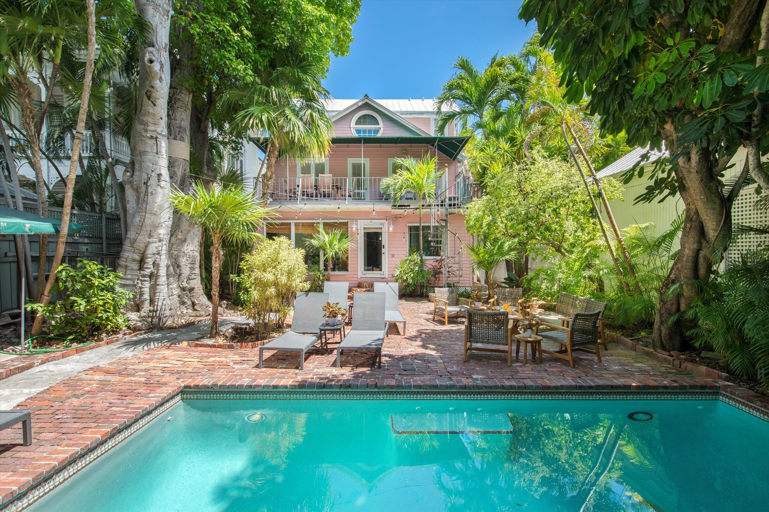 A pool area with a brick patio, lounge chairs, and a dining set.
