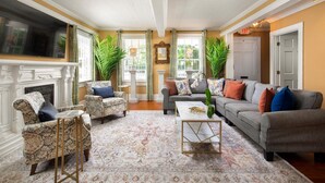 A living room with a fireplace, a sofa set, patterned rug, and large windows with curtains. - William Skelton Home - Sleeps 16 just off Duval St (Key West)