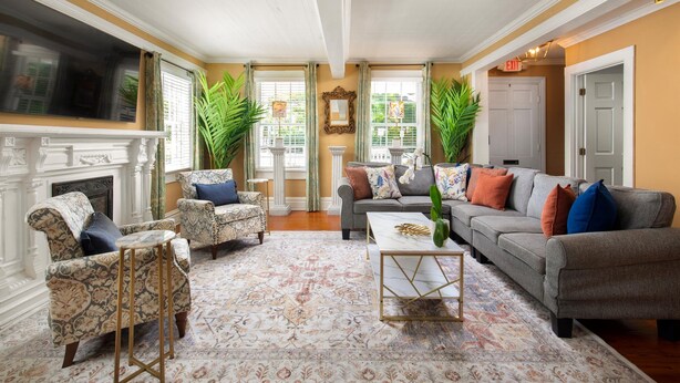 A living room with a fireplace, a sofa set, patterned rug, and large windows with curtains. - William Skelton Home - Sleeps 16 just off Duval St (Key West)