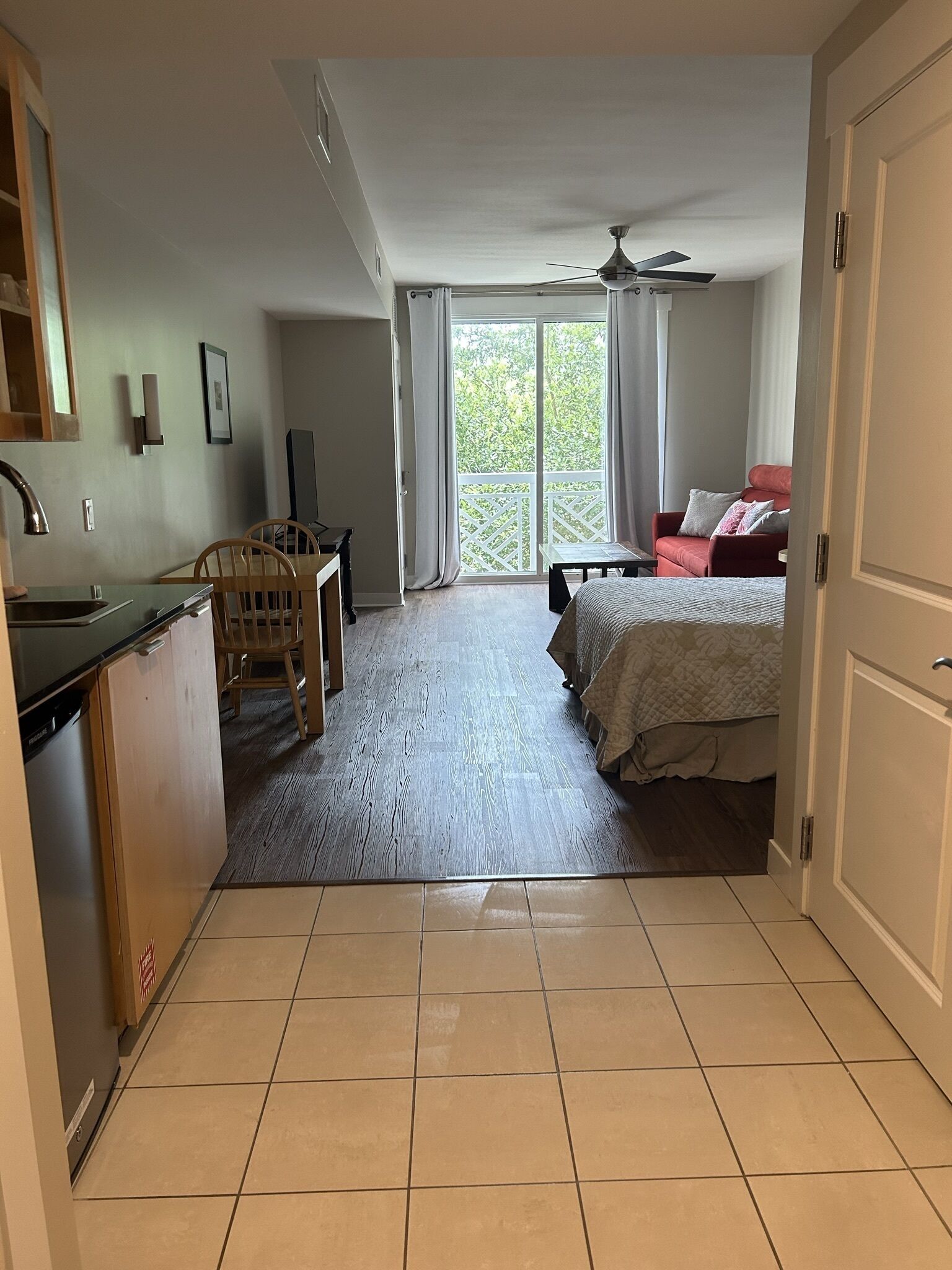 A compact room with a kitchenette, a dining area, a bed, and a sliding glass door leading to a balcony.
