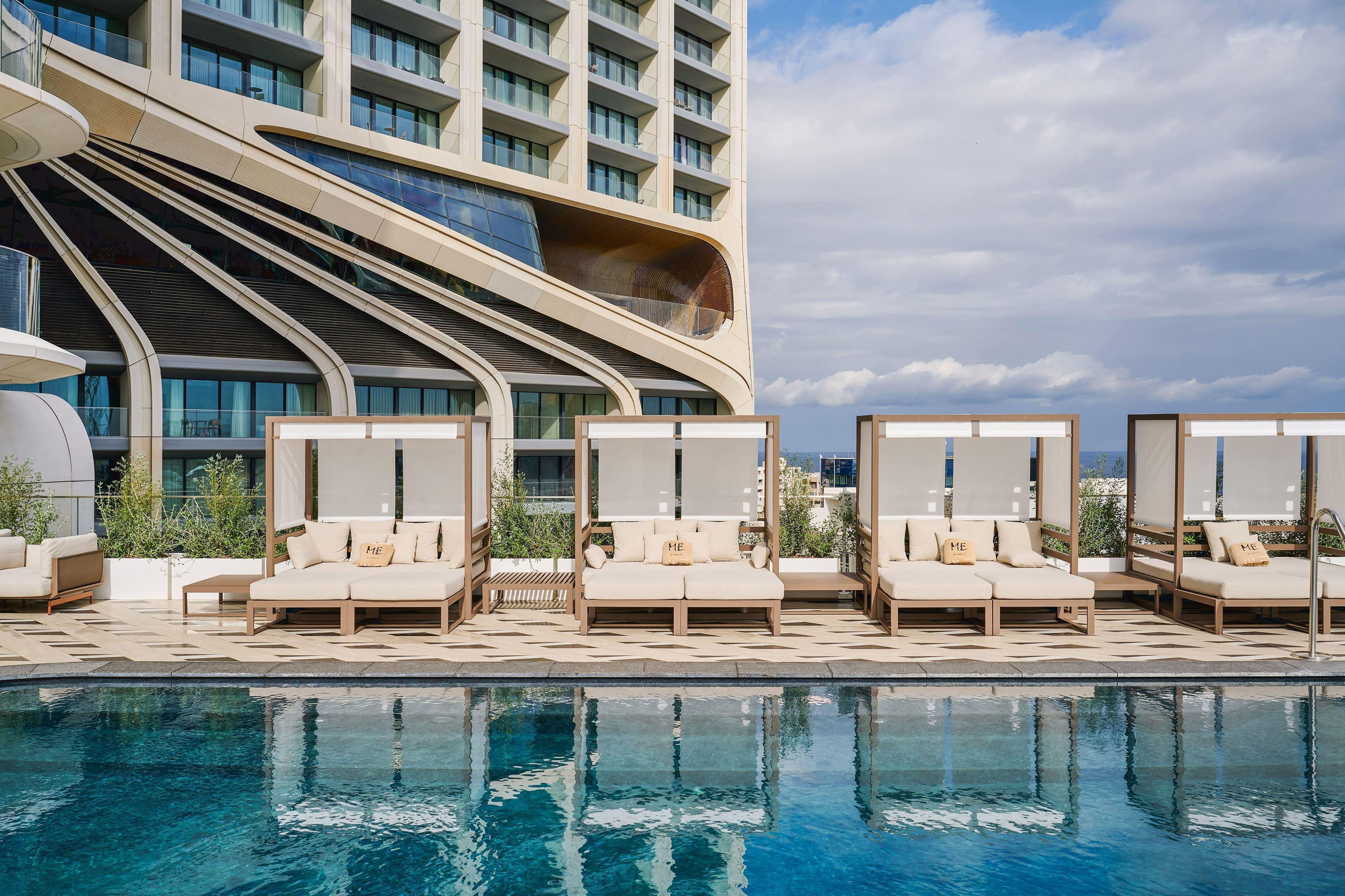 Um hotel moderno com área de piscina, espaço ao ar livre para sentar e uma fachada curva marcante.