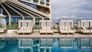 Un hotel moderno con zona de piscina, mobiliario exterior y una fachada curva distintiva.