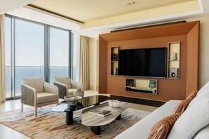 A modern living room with a large TV, comfortable seating, and a view of the ocean.