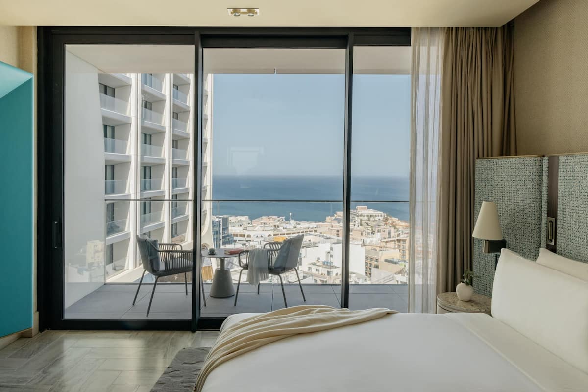 A hotel room with a large sliding glass door leading to a balcony with a city view.