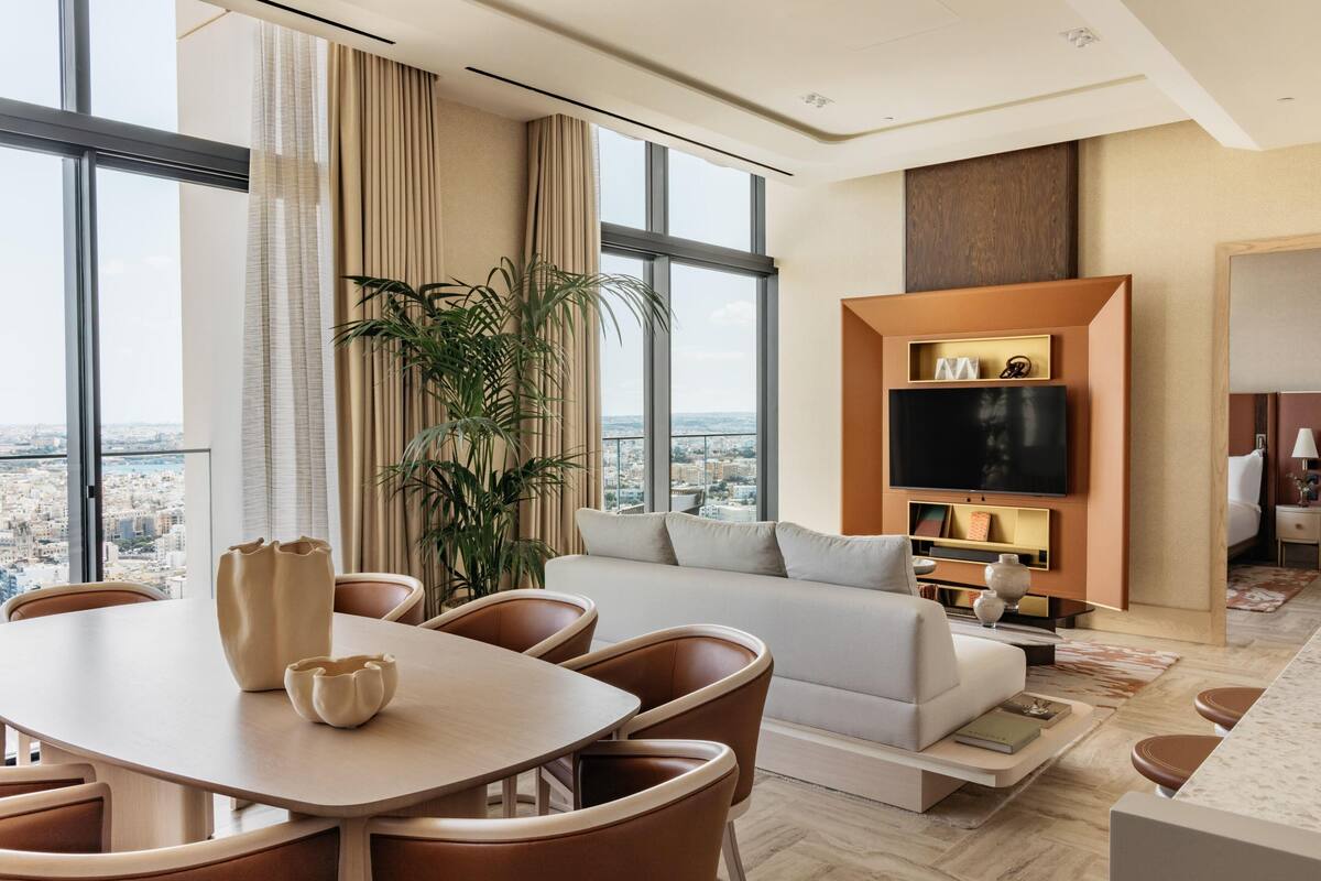 A modern living room with a large window, a sofa, a TV, and a dining area.