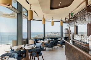 Un restaurante moderno con mesas redondas, sillas tapizadas en azul y una zona de bar con cristalería.
