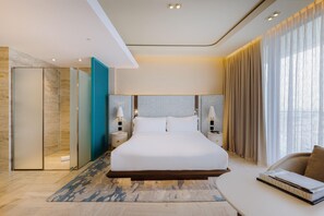 A modern hotel room with a large bed, a sitting area, and a bathroom with a glass shower enclosure. - Me Malta (St. Julian's)