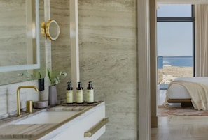 A bathroom with a marble countertop, a gold faucet, a mirror, and toiletries.