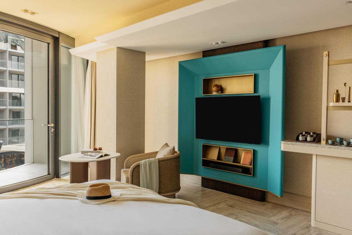 A modern hotel room with a large bed, a television mounted on a teal wall, a small round table, and a chair.