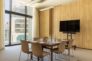 A conference room with a large table, chairs, a flat-screen TV, and a view of a building through large windows.