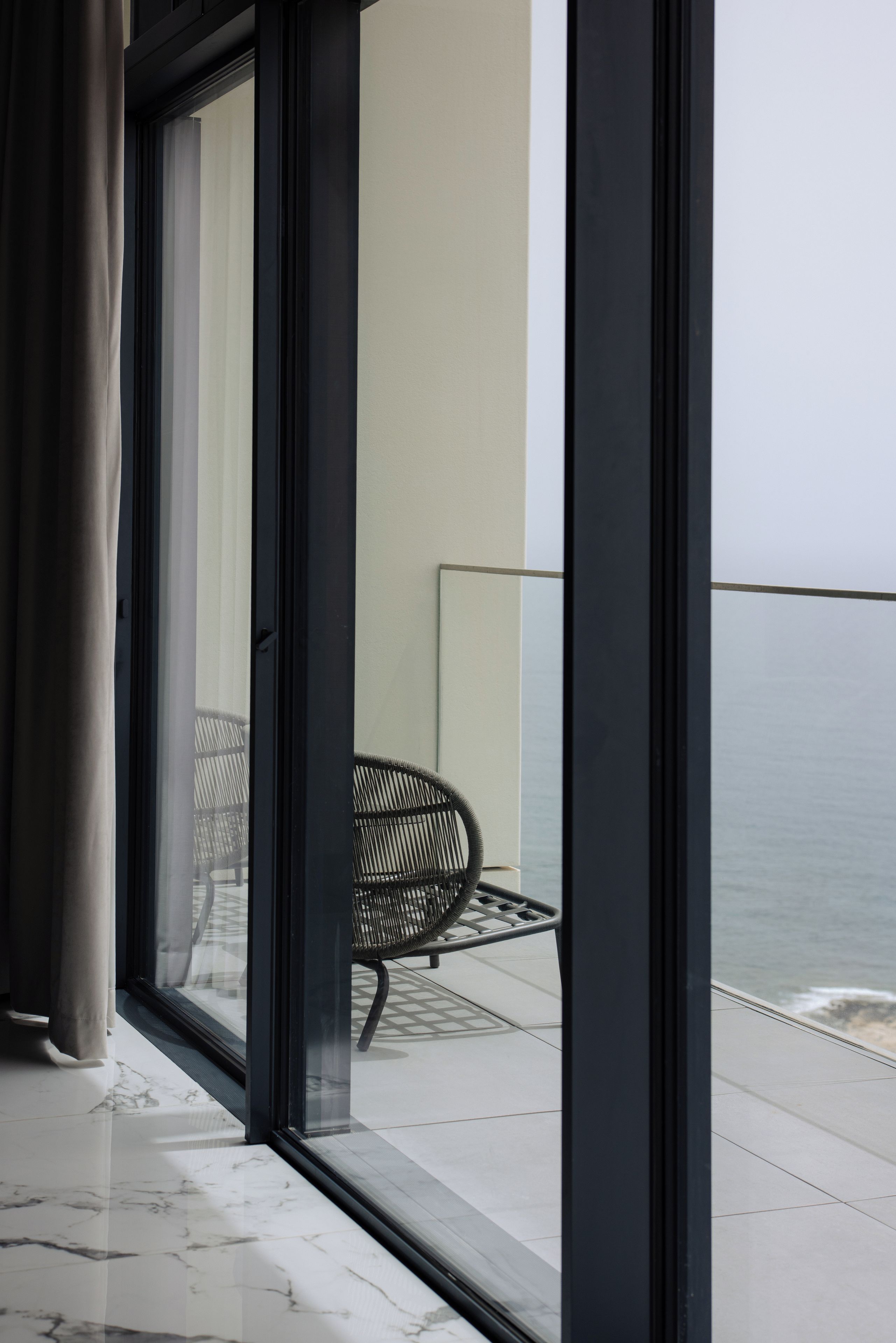 Un interior moderno con un amplio ventanal corredera que da a un balcón con vistas al mar.