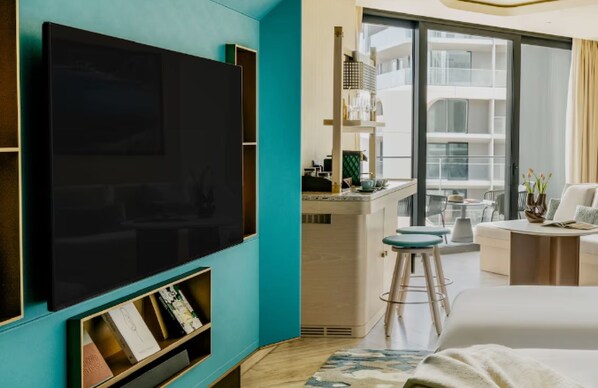A modern hotel room with a large flat-screen TV, a balcony with a dining area, and a view of the building's exterior. - Me Malta (St. Julian's)