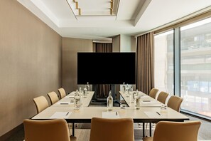A conference room with a long table, chairs, a large screen, and a city view. - Me Malta (St. Julian's)