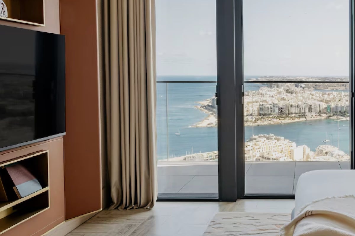 A bedroom with a large window, a TV, and a bookshelf.