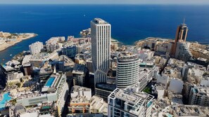A coastal cityscape with high-rise buildings, a marina, and a clear view of the sea.