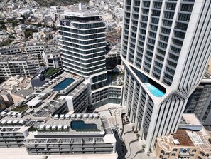 Un moderno edificio de gran altura con piscina en la azotea, varios balcones y un diseño curvo característico.