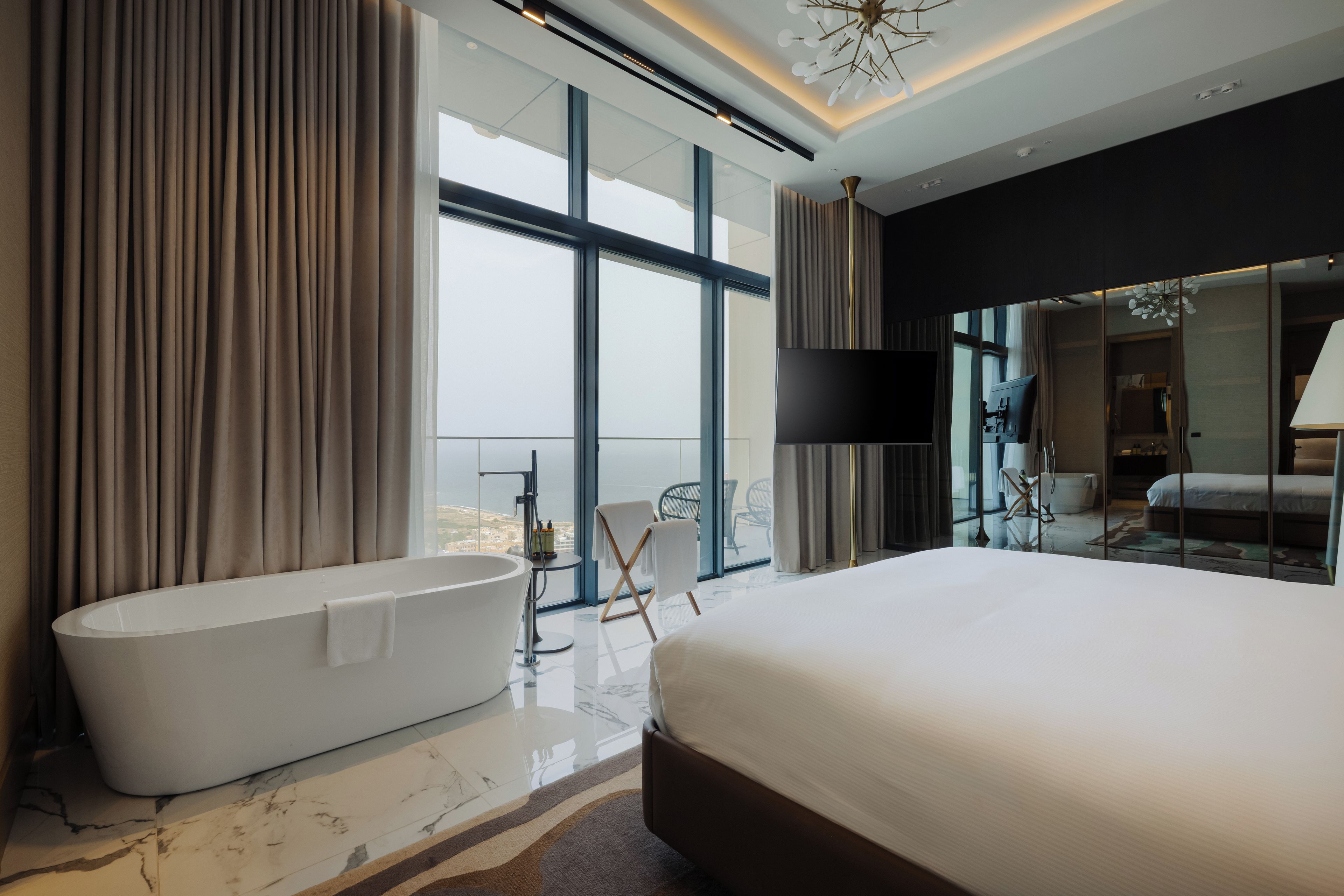 Ein modernes Hotelzimmer mit einem großen Bett, einer freistehenden Badewanne und einem Balkon mit Blick.