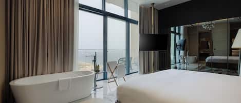 A modern hotel room with a large bed, a freestanding bathtub, and a balcony with a view.