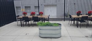 Outdoor seating area with tables and chairs, surrounded by potted plants and a tile-paved ground.