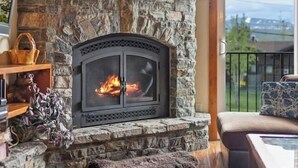 Ein Kamin aus Stein mit Feuer, Holzboden, eine Couch und Blick durch eine Glastür.