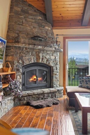 A stone fireplace with a fire, wooden flooring, a sofa, and a view through a glass door. - Tahoe Townhome: Steps to Lake/Pool/Hot Tub (Dollar Point)