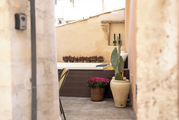 Un estrecho pasillo exterior con una maceta de cactus, una cesta de mimbre con flores rosadas y un jarrón grande.