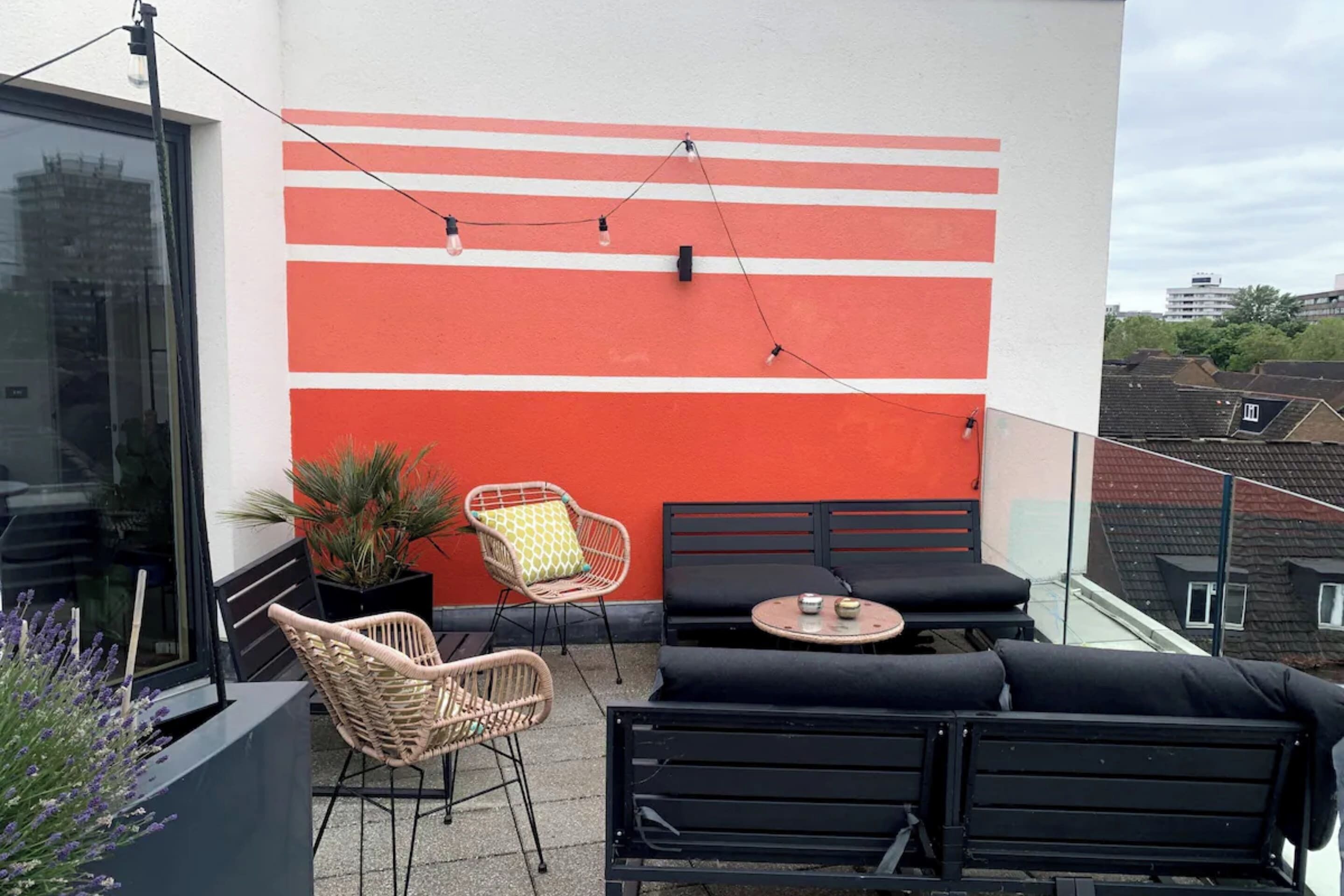 A balcony with a red and white wall, wicker chairs, black sofas, and a small table.