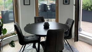 Uma sala de jantar com mesa redonda, seis cadeiras, um objeto decorativo no centro e um lustre.