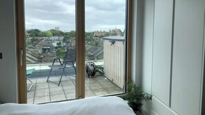 Quarto com uma grande porta de vidro deslizante que dá para uma varanda com vista para a paisagem urbana.