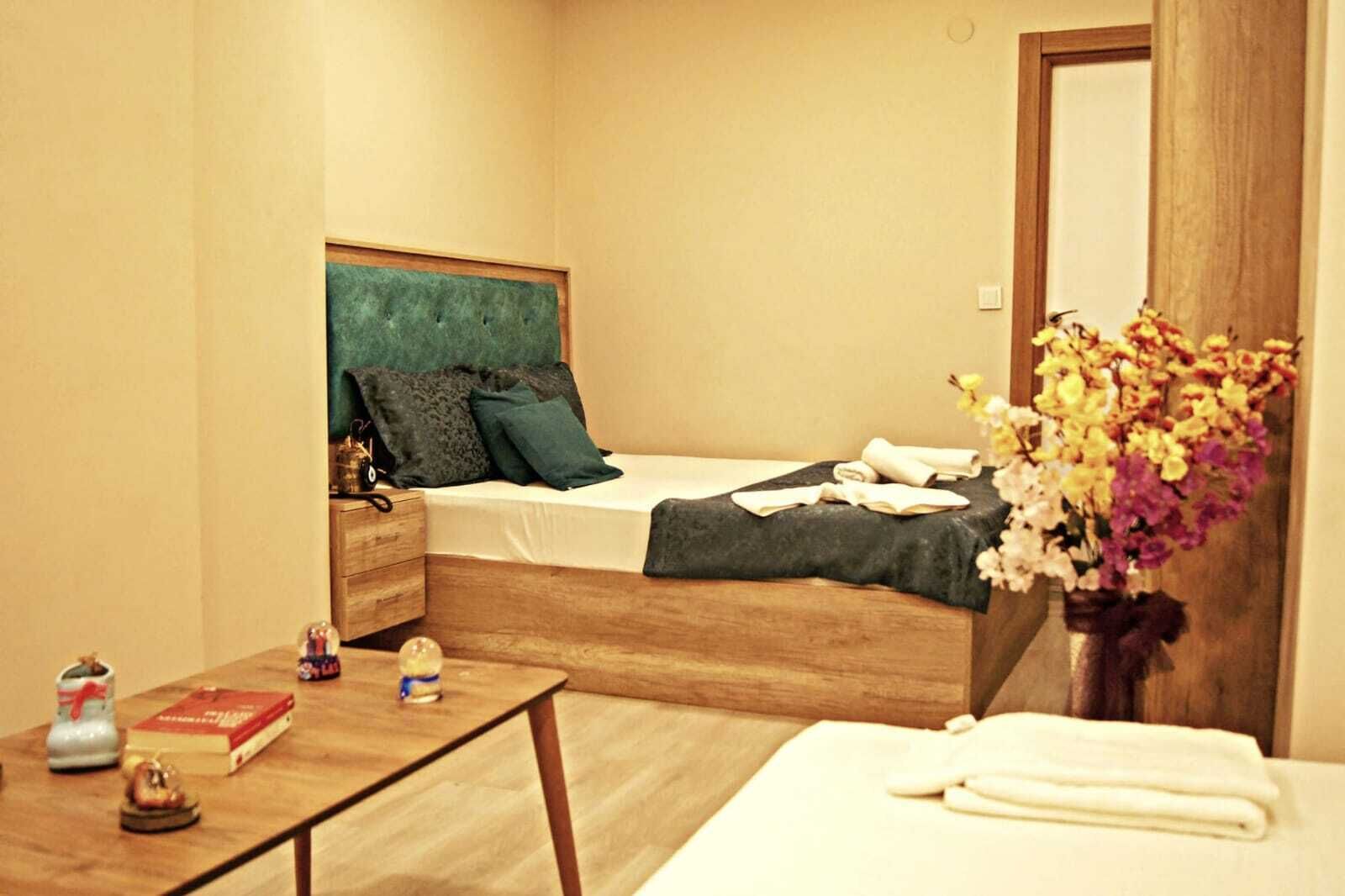 A bedroom with a wooden bed, a nightstand, a bedside table with books and a small figurine, and a vase with flowers.