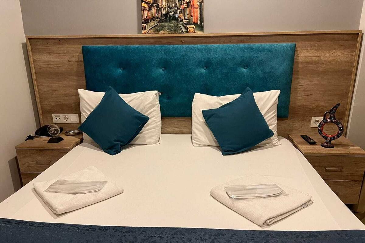 A hotel room with a large bed, two nightstands, a wooden headboard, and a painting above the bed.