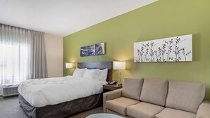 Ein Hotelzimmer mit Bett, Sofa, Pouf, zwei Nachttischlampen und Bildern an den Wänden.