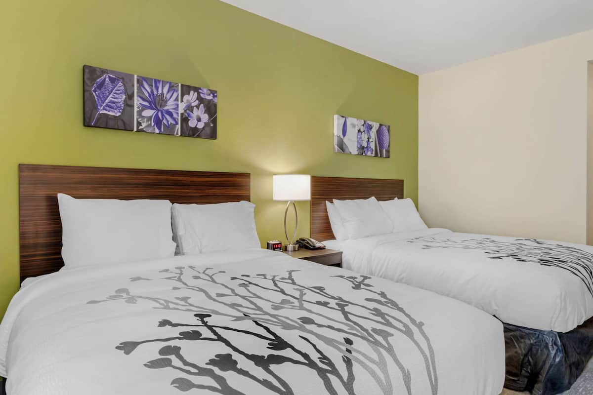 A hotel room with two beds, a wooden headboard, a nightstand with a lamp, and floral artwork on the walls.