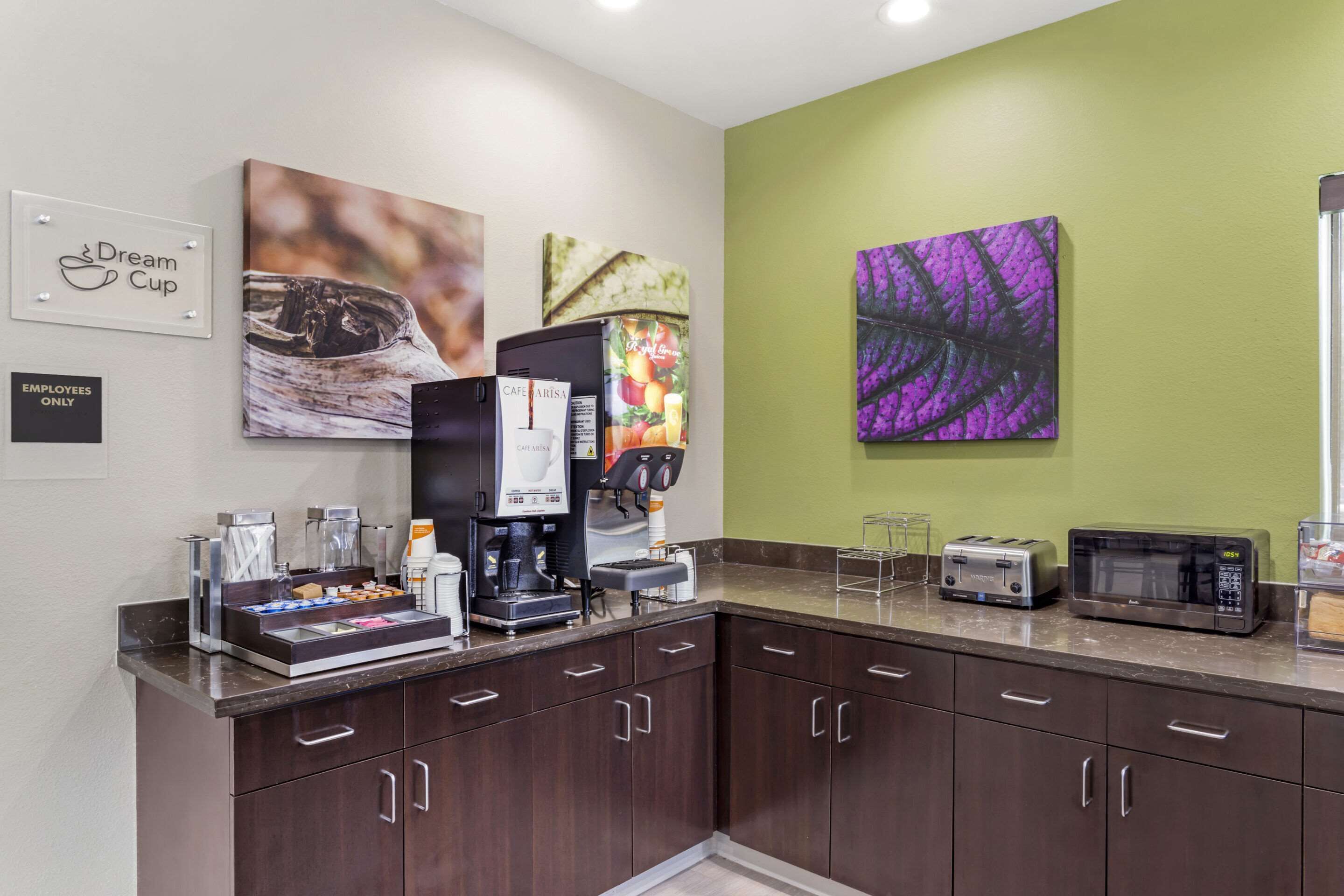 Una kitchenette equipada con cafetera, tostadora y microondas. Se observan armarios y una encimera.