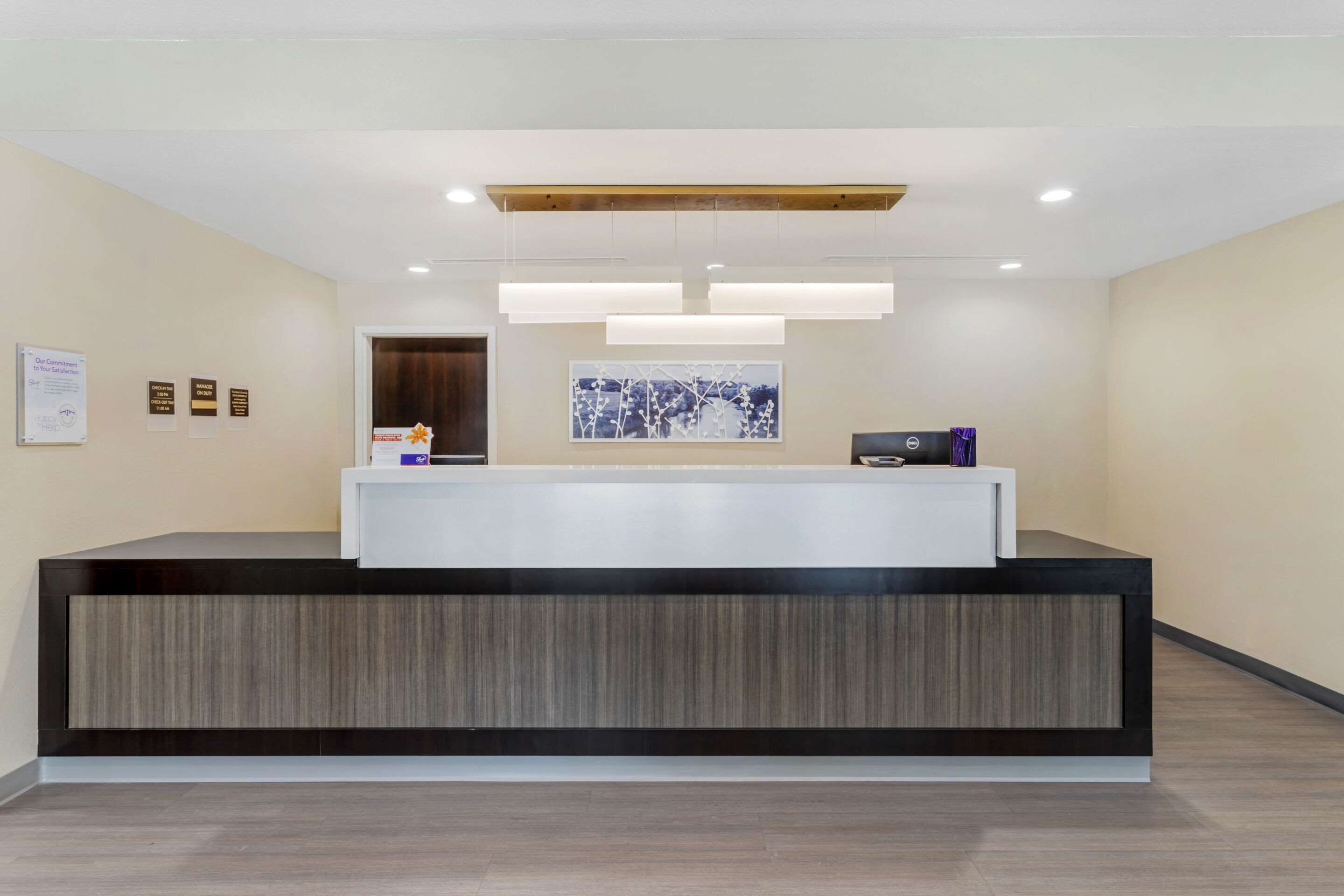 A reception area with a modern reception desk, a framed artwork on the wall, and a wooden ceiling beam.