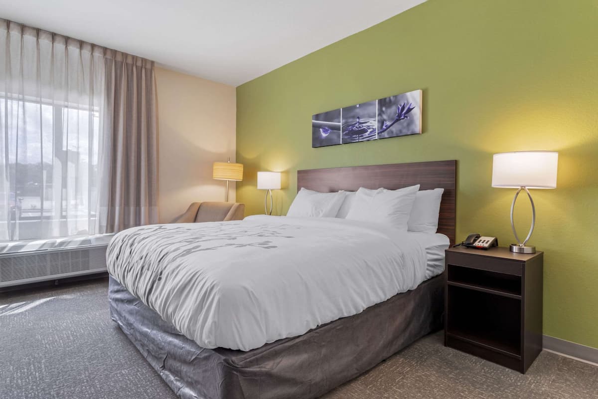 A hotel room with a large bed, two bedside lamps, a nightstand, a chair, and a window with curtains.
