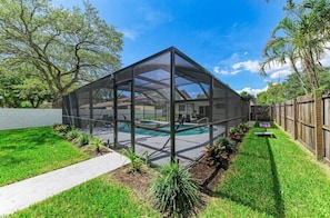 A covered outdoor area with a pool, surrounded by a wooden fence and greenery.