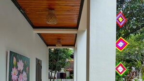 A covered outdoor area with a wooden bench, a wall-mounted painting, and a view of a gated entrance leading to a street. - Lotus Corner - Heritage B&B (Luang Prabang)
