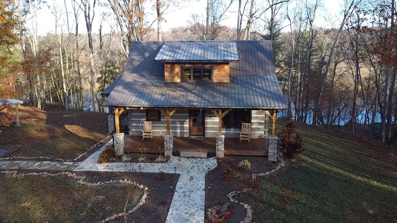 A rustic cabin with a stone foundation, wooden porch, and a metal roof.