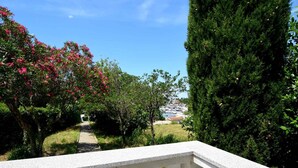 En balkon med stenvangsmur, udsigt over en have med lyserøde blomster og grønne træer.