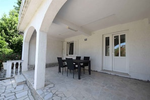 Un espacio al aire libre cubierto con piso de piedra, una mesa con sillas y una puerta blanca.