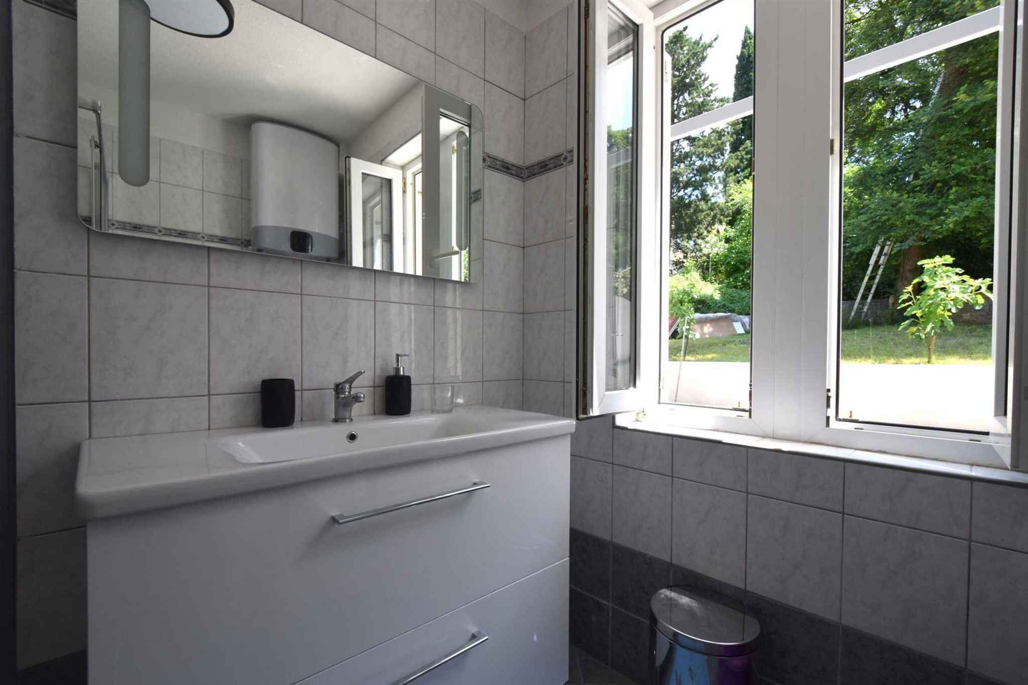 A bathroom with a sink, mirror, and window.