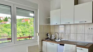 A modern kitchen with white cabinets, a wooden countertop, and a window overlooking a green landscape. - Holiday apartment mit Klimaanlage und Balkon (Jadranovo)