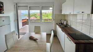 A modern kitchen with white cabinets, a wooden countertop, and a view of a green landscape through the windows. - Holiday apartment mit Klimaanlage und Balkon (Jadranovo)