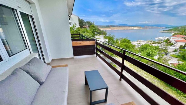 A balcony with a sofa, a small table, and a view of a body of water and distant landscape. - Holiday apartment mit Klimaanlage und Balkon (Jadranovo)